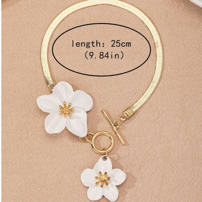 Gold bracelet with white floral charms on a beige background