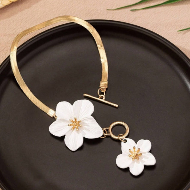Gold necklace with white floral pendants on a black plate
